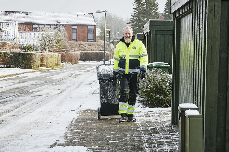 Skraldemand trækker affaldsbeholder hen ad fortov, der er ryddet for sne.