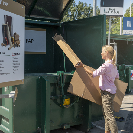 Kvinde afleverer pap i container på genbrugsstationen.