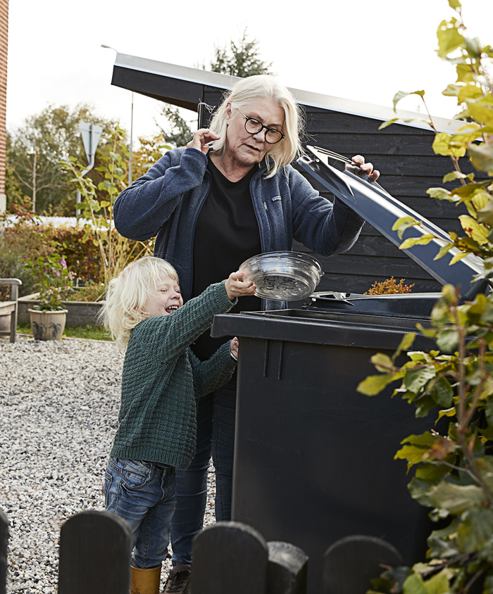 Bedstemor og barn putter plast i beholderen til genanvendeligt affald.