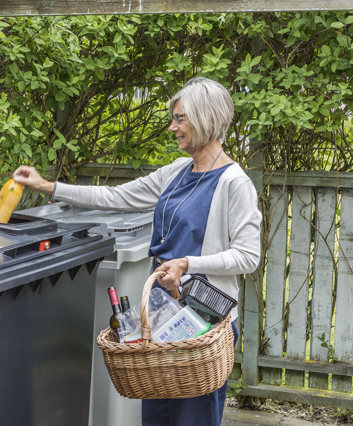 Kvinde afleverer glas og plast i fælles beholder til genanvendeligt affald.