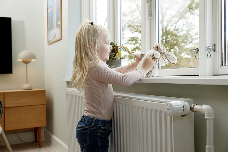 Pige står ved radiator