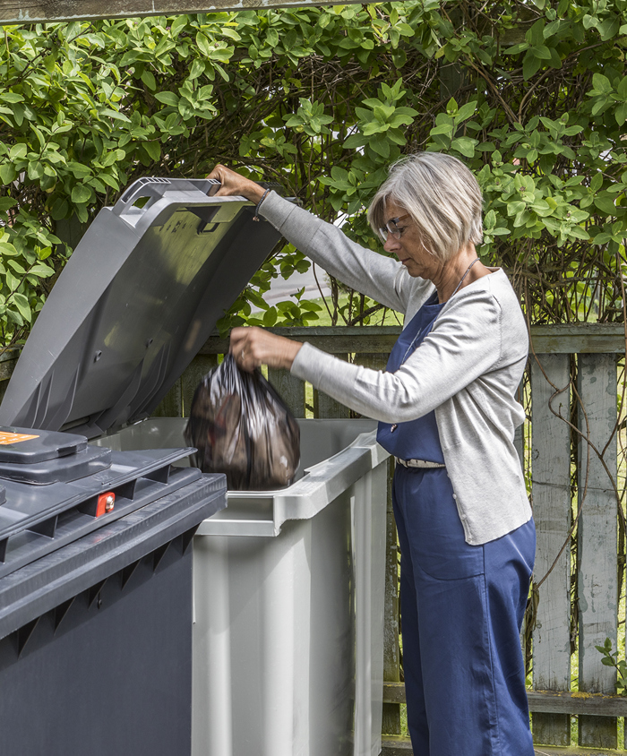Kvinde afleverer restaffald i fælles beholder.