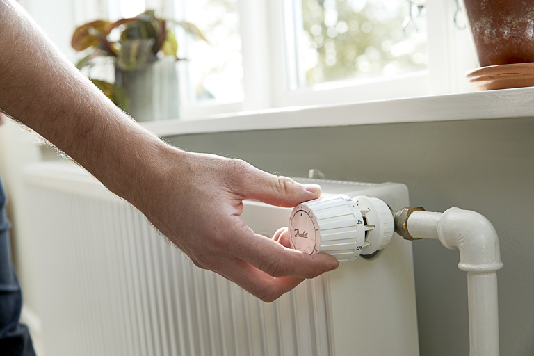Person justerer termostat på radiator