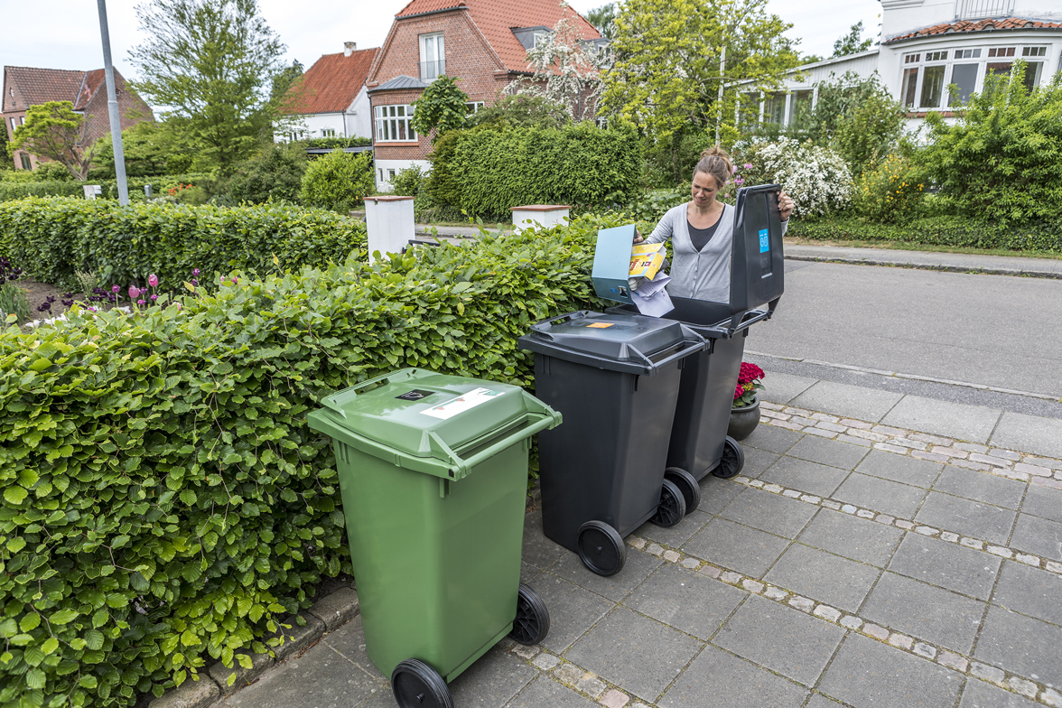 Kvinde hælder pap og papir i beholderen til genanvendeligt affald.