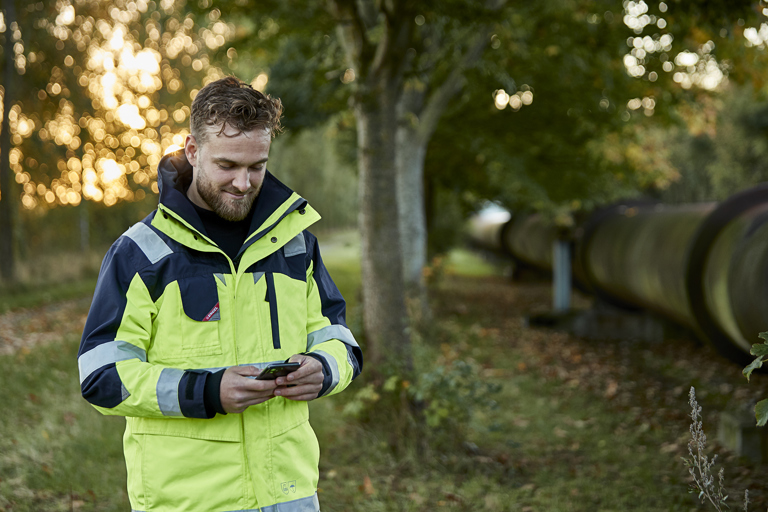 Medarbejder ved fjernvarmerør kigger på sin mobil