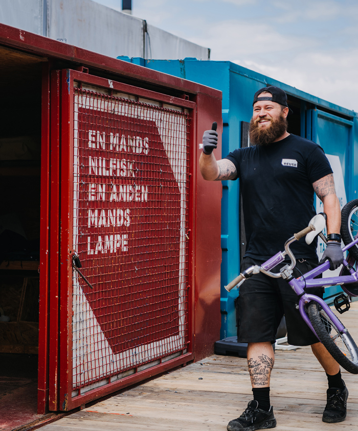 Glad medarbejder på REUSE bærer børnecykel ind i container.
