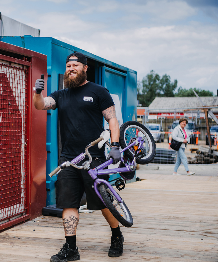 Glad medarbejder på REUSE bærer børnecykel ind i container.