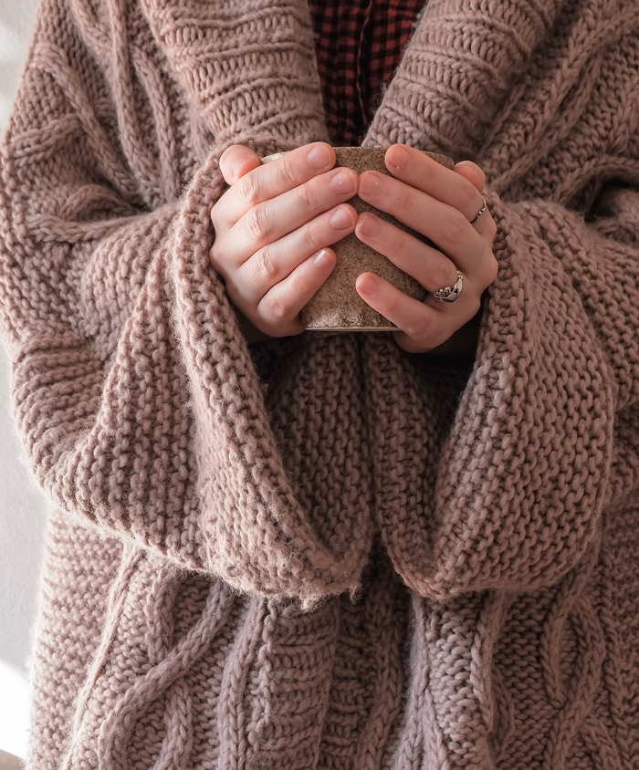 Kvinde i strikket trøje med tekrus i hænderne