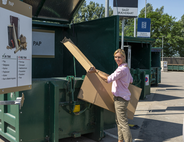 Kvinde afleverer pap i container på genbrugsstationen.